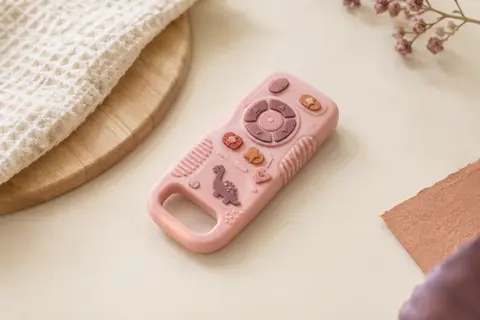 Anneau de dentition rose en silicone, en forme de télécommande avec boutons en relief et motif dinosaure.