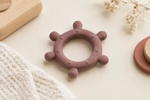 Anneau de dentition rond en silicone présenté sur un fond crème avec du coton gaufré et du bois clair.