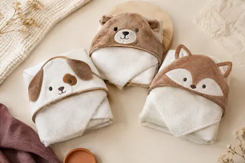 Lot de trois capes de bain bébé à capuche, au motif animal brun et blanc, posées sur un fond crème