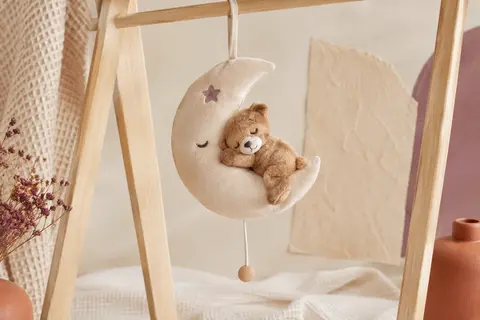Boîte à musique en velours représentant un ourson dans la lune, suspendue dans un décor doux et lumineux