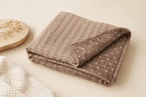 Couverture bébé Bearmoss en mousseline brune, pliée pour montrer son envers doux à pois.