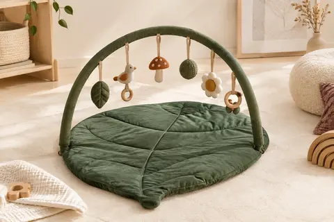 Tapis d’éveil vert forêt en forme de feuille avec arche amovible et six jouets suspendus sur fond crème.