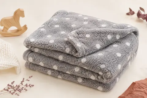 Couverture bébé grise à motif de pois, pliée sur un fond crème près d’un élément en bois clair.