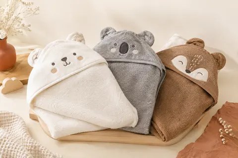 Trois capes de bain bébé en bambou à capuche et motifs animaliers, présentées sur un fond crème