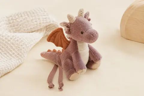 Mini boîte à musique Fehn en peluche dragon, avec ses deux rubans posés sur un fond crème