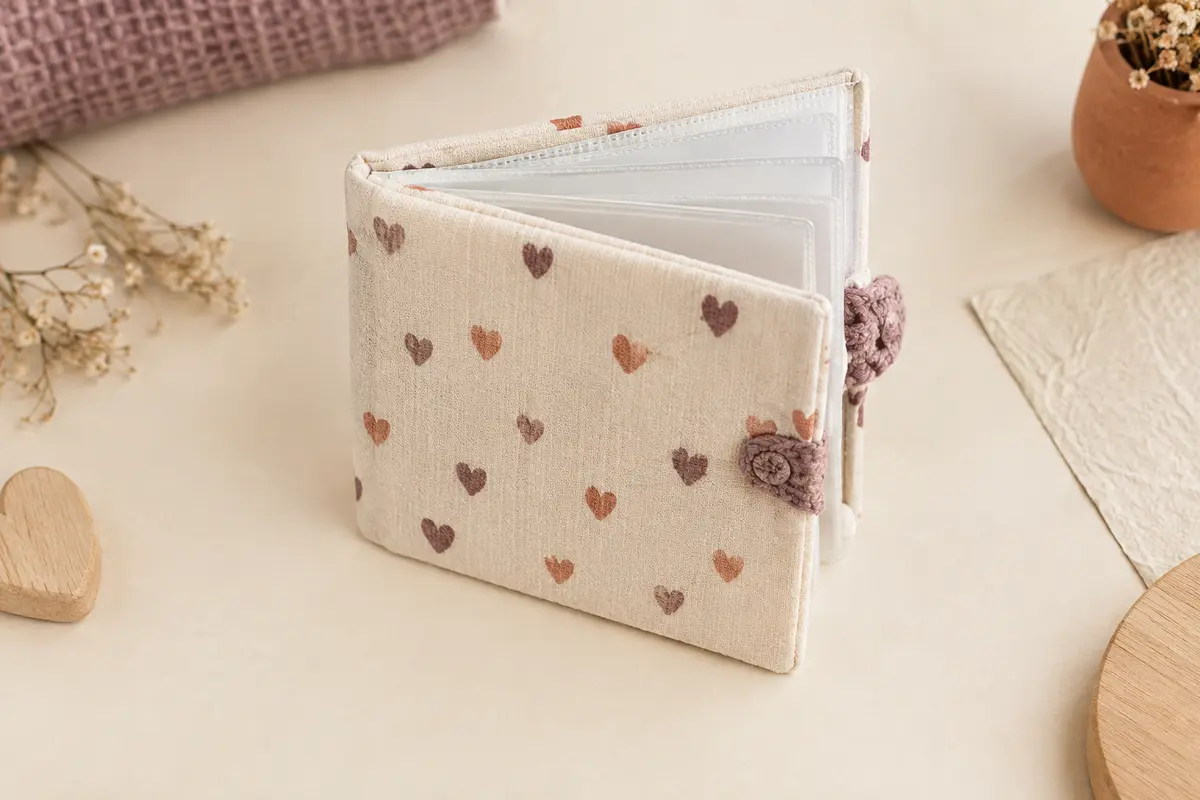 Petit album photo bébé en tissu à motif de cœurs, entrouvert pour montrer ses pochettes transparentes.