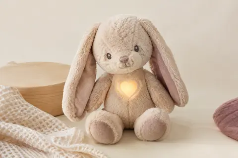 Peluche lapin apaisante à tête mobile et cœur lumineux, posée sur un fond crème près de bois clair