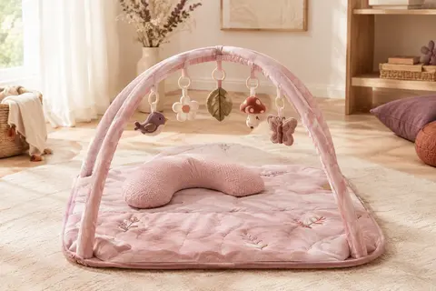Tapis d’éveil rose avec arche amovible, cinq jouets suspendus et coussin de soutien sur fond clair.