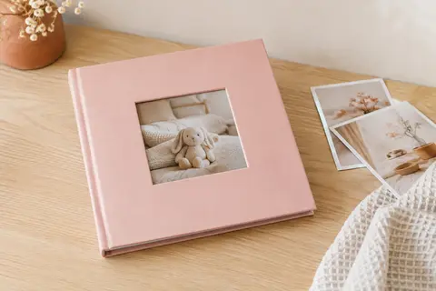 Album bébé rose pastel à pochettes, posé près de quelques tirages photo et d’un tissu gaufré
