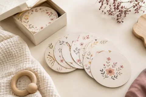 Cartes étapes bébé à motifs floraux disposées près de leur boîte sur un fond crème et du coton gaufré.