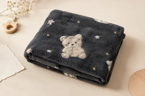 Couverture bébé anthracite avec motif d’ourse en relief, pliée sur un fond crème lumineux