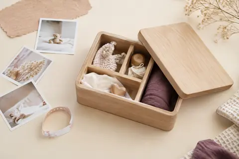 Boîte à souvenirs bébé en bois avec couvercle, posée sur un fond crème près de photos et d’un bracelet de maternité.