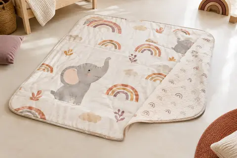 Tapis de jeu bébé réversible aux motifs éléphant et arc-en-ciel, déplié sur un sol clair
