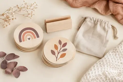 Cartes étapes bébé rondes en bois avec leur support et leur pochette textile, disposées sur un fond crème.