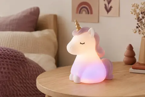 Veilleuse licorne en silicone posée sur une table en bois clair dans une chambre aux tons doux