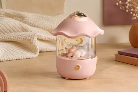 Veilleuse projecteur rose avec compartiment transparent et lapin décoratif, posée sur une table en bois clair