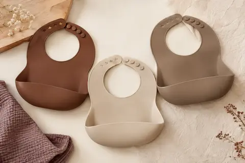 Trois bavoirs bébé en silicone, avec poche profonde et tour de cou réglable, dans des tons doux.
