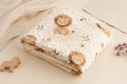 Couverture bébé en polaire Minky écrue avec motif de lion aquarelle, pliée sur un fond crème