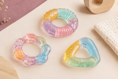 Trois anneaux de dentition souples multicolores posés sur un fond crème près d’un tissu gaufré.