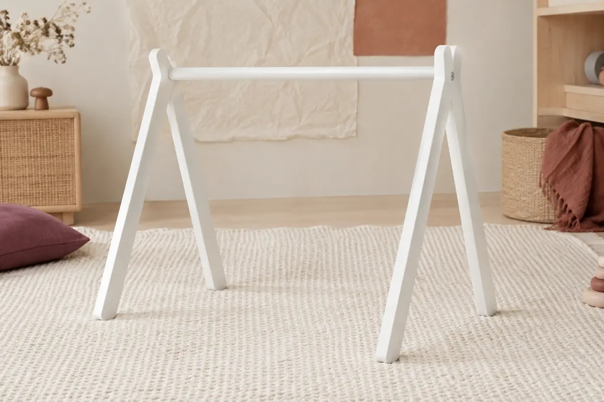 Portique d’éveil en bois laqué blanc, sans jouets suspendus, posé sur un tapis crème dans un décor doux.