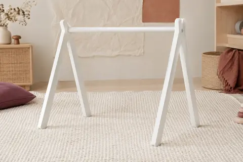 Portique d’éveil en bois laqué blanc, sans jouets suspendus, posé sur un tapis crème dans un décor doux.
