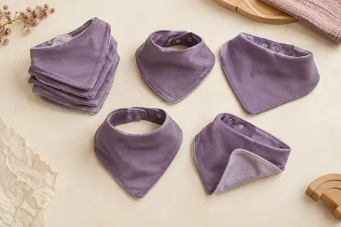 Lot de six bavoirs bandana violets en coton, pliés sur un fond crème près d’une surface en bois clair.