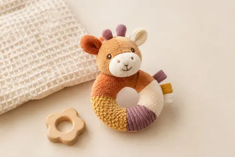 Hochet en peluche multicolore avec textures variées, présenté sur un fond crème près de coton gaufré.