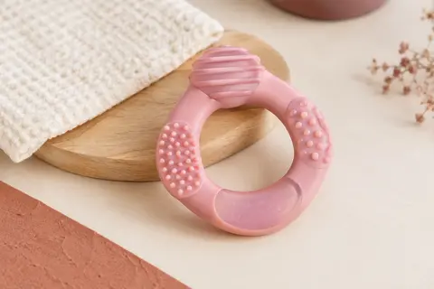 Anneau de dentition réfrigérant rose Suavinex avec reliefs, posé sur un fond crème près d’un support en bois clair