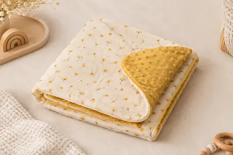 Couverture bébé en coton et Minky présentée sur un fond crème près d’un tissu gaufré et de bois clair.