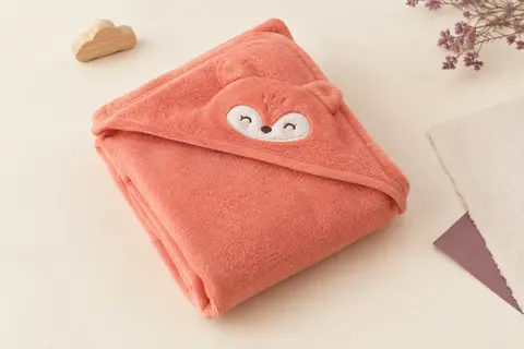 Cape de bain bébé en polaire corail avec capuche brodée d’un motif animalier, posée sur un fond crème.