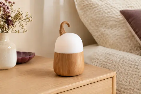 Veilleuse tactile à effet grain de bois posée sur une table de chevet en bois clair.